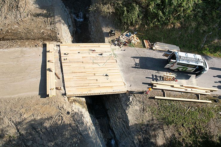 Luftaufnahme der neuen Brücke aus Holz; daneben ein Auto der Baufirma; neben der BRücke liegen noch Werkzeuge und Bretter