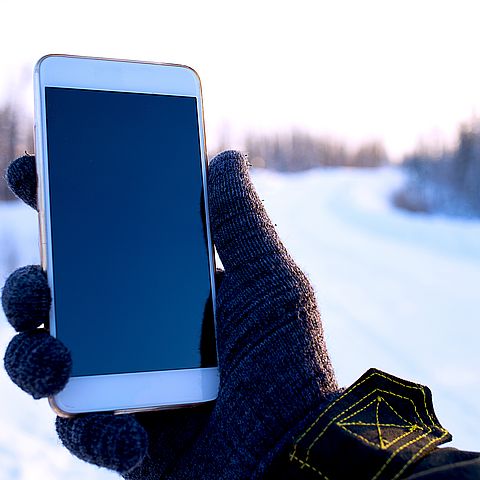 Hand hält Mobiltelefon in einer winterlichen Umgebung