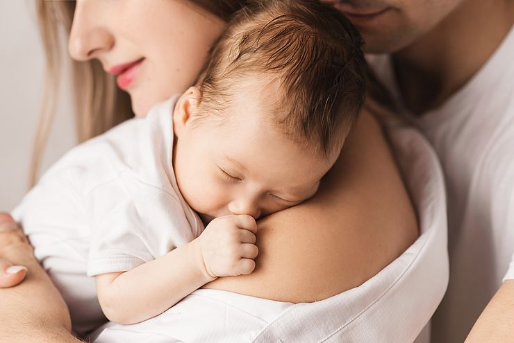 Symbolbild junger Eltern mit Baby auf dem Arm