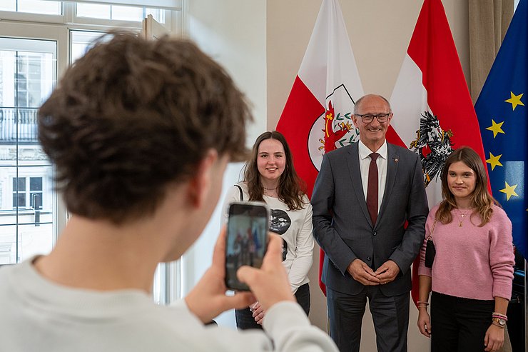 Schüler macht Foto von LH mit zwei Schülerinnen vor Fahnen.