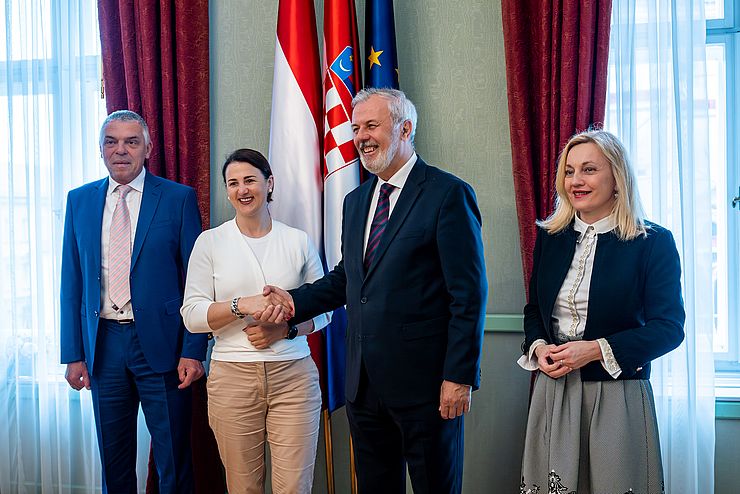 Gruppenfoto: Mair und Sanader in der Mitte, schütteln einander die Hand; im Hintergrund Fahnen von Österreich, Kroatien und der EU