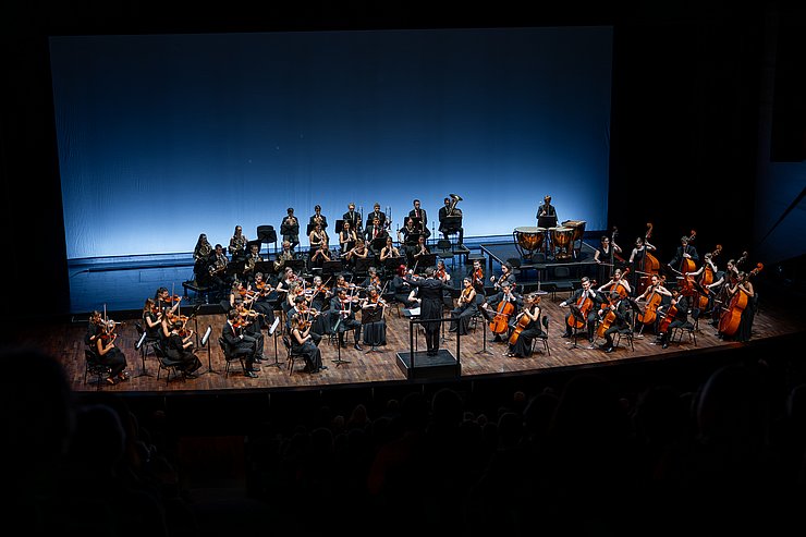 Aufnahme eines Symphonieorchesters, das Bild ist schwarz umrandet.