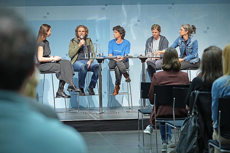 © Land Tirol/Trenker Menschen sitzen an Tisch mit Mikrofon vor Publikum