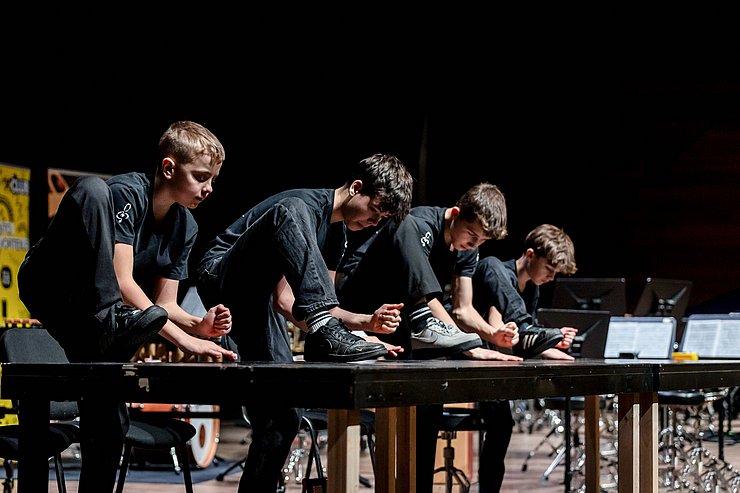 Vier Buben klopfen auf einen Tisch.