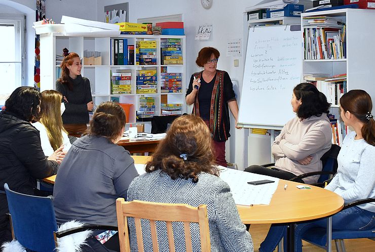 Die Teilnehmerinnen des Deutschkurses sitzen an einem großen runden Tisch; die Kursleiterin steht an der Tafel