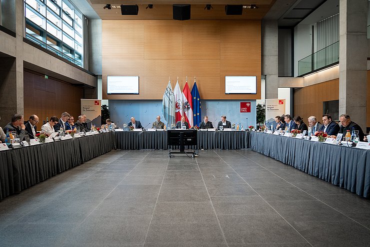 © Land Tirol/Neuner Mehrere Personen sitzen im großen Saal in einer U-Form.