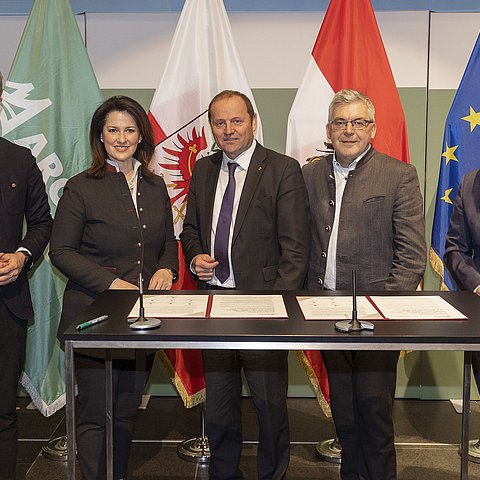 Gruppenbild der LandesrätInnen vor Fahnen, auf dem Tisch liegen Dokumente zur Unterzeichnung