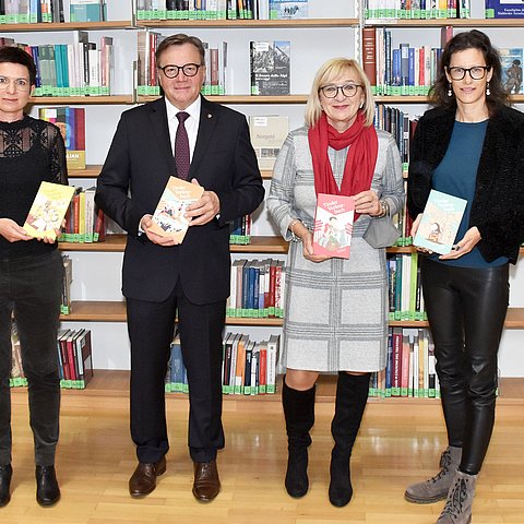 Autorin Carolina Schutti, Landeshauptmann Günther Platter, Bildungslandesrätin Beate Palfrader und Fachgruppenobfrau der Buch- und Medienwirtschaft Tirol Sonja Altenburger vor einer Bücherwand mit den 4 Tiroler Vorlesebüchern in Händen