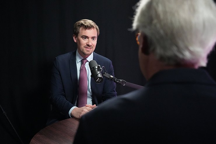 © Land Tirol/Trenker Zwei Männer sitzen sich am Tisch gegenüber. Einer mit Podcast-Mikrofon.