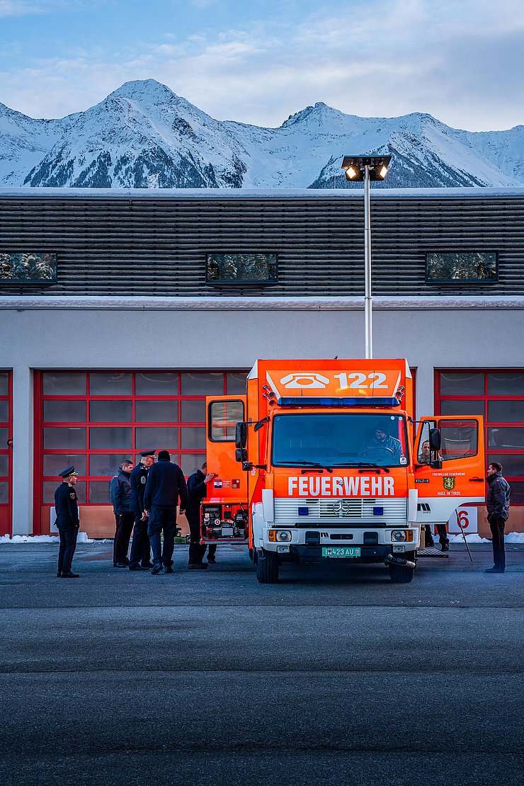 Feuerwehrauto steht vor Garage; Feuerwehrleute in Uniform stehen neben dem Auto und sehen hinein