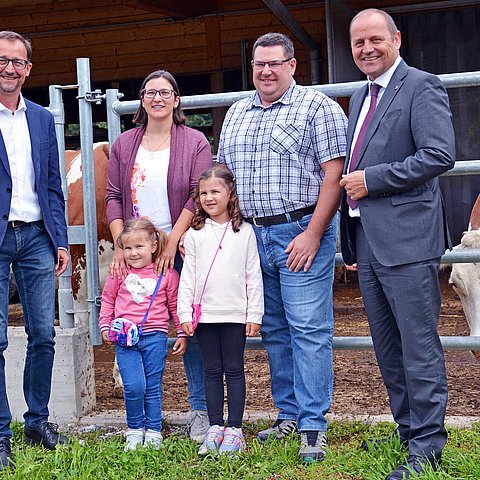 Auf dem dem Bild sind LHStv Josef Geisler (1.v.re.) und Thomas Danzl, Geschäftsführer vom Landeskulturfonds (1.v.li.) mit Georg und Manuela Kapferer sowie den zwei Töchtern Franziska (rechts) und Michaela zu sehen. Im Hintergrund sieht man den Kuhstall der Familie.