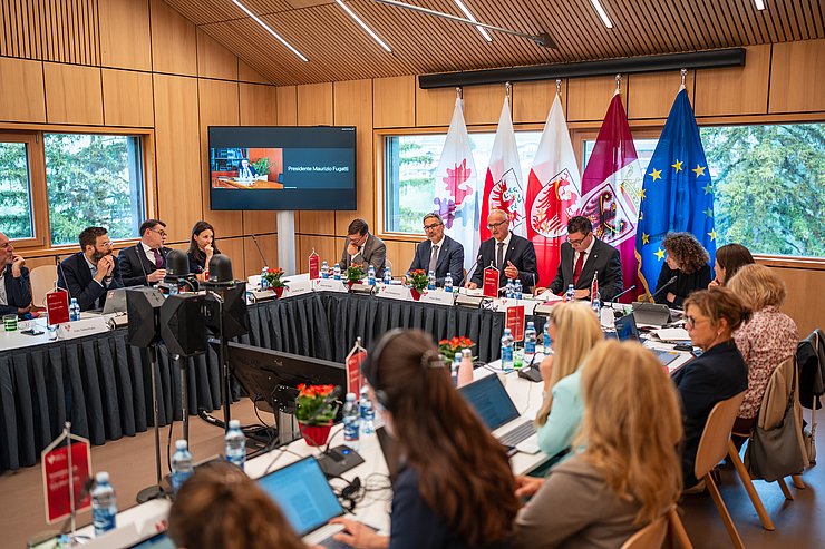 © Land Tirol/Fitsch Personen sitzend, dahinter Fahnen