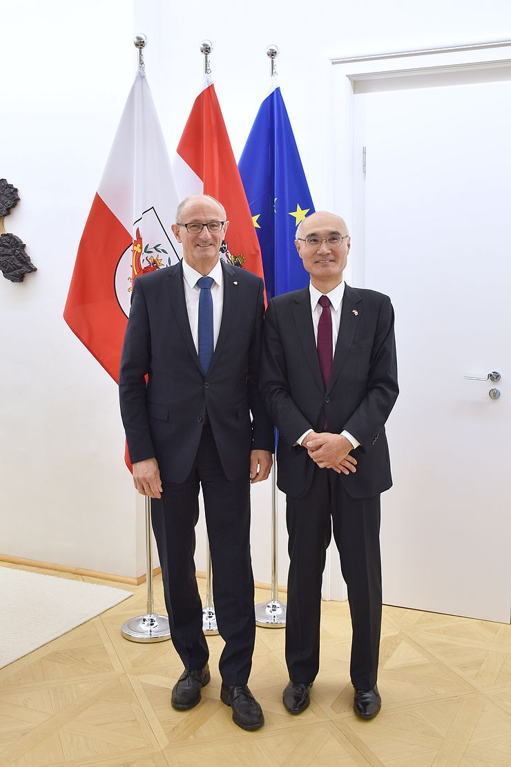 Landeshauptmann Anton Mattle steht neben japanischem Botschafter Akira Mizutani; im Hintergrund sind Fahnen