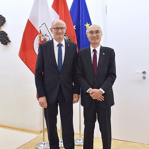 Landeshauptmann Anton Mattle steht neben japanischem Botschafter Akira Mizutani; im Hintergrund sind Fahnen