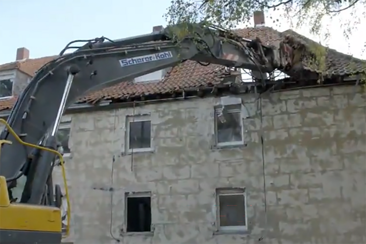 Ein großes altes großes Haus wird mit einem Bagger abgerissen.