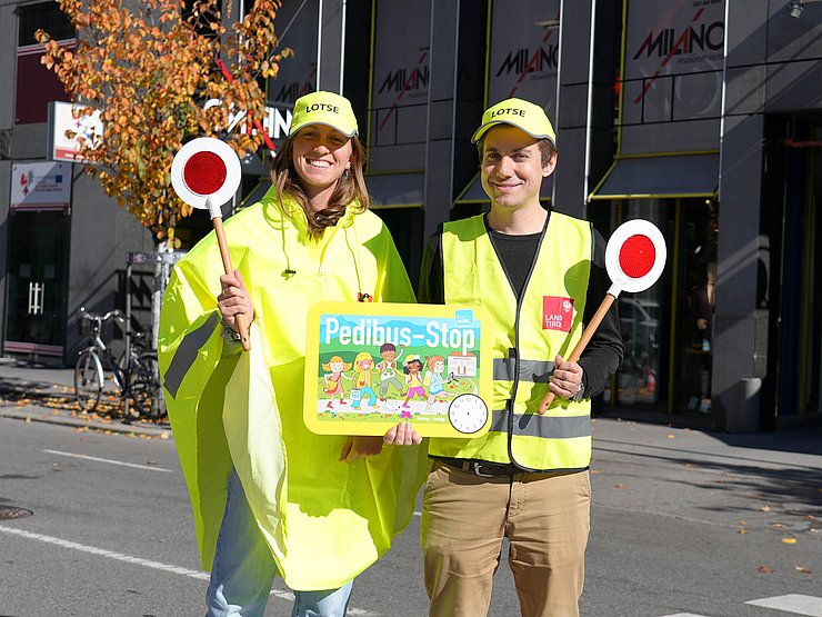 Zwei Menschen mit Warnwesten und einem Pedibus-Schild