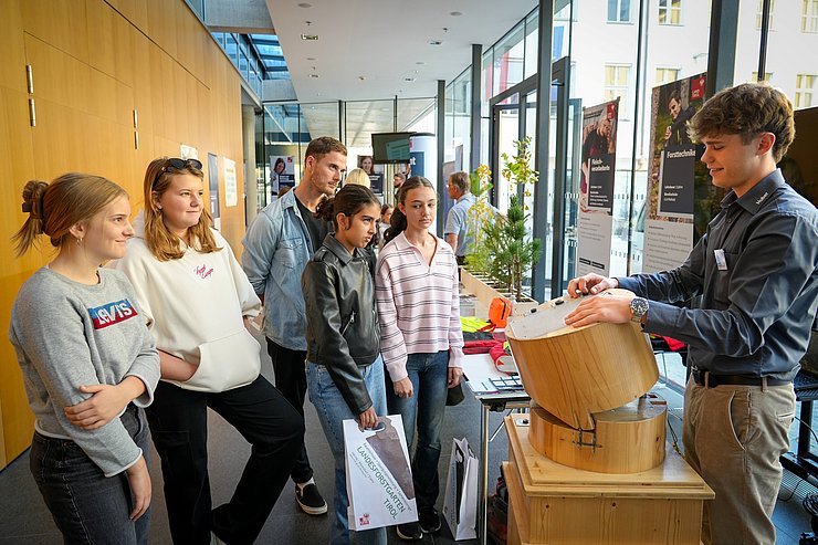 © Land Tirol/Saxl Schülerinnen und Schüler stehen im Halbkreis nebeneinander und hören dem Lehrling der Forstabteilung zu.
