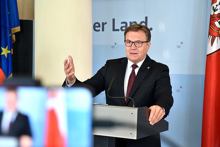 Landeshauptmann Günther Platter steht vor einer Kamera und hebt seine Hand.