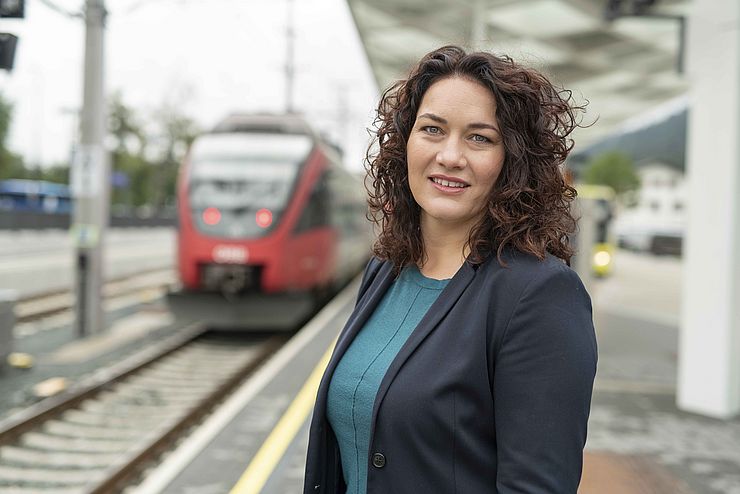 Landeshauptmann-Stellvertreterin Ingrid Felipe steht auf einem Bahnsteig mit einem Zug und einem Bus im Hintergrund.