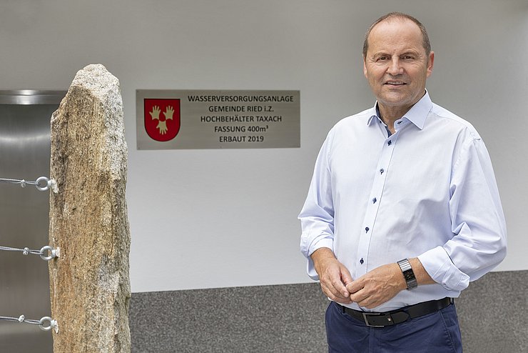 Bild von LHStv Josef Geisler vor einem Gebäude. Im Hintergrund ist ein Schild zu sehen, auf welchem Wasserversorgungsanlage Gemeinde Ried i. Z. zu lesen ist