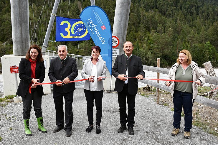 Personen durchschneiden rotes Band vor Brücke