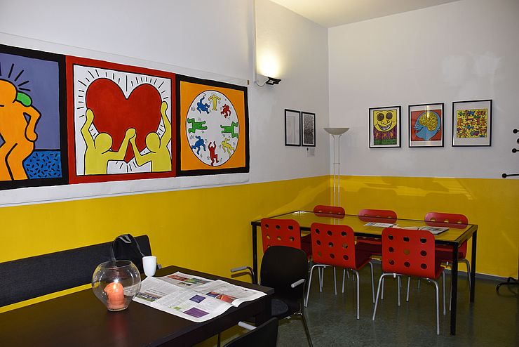 Leerer Raum mit Tischen und Stühlen, an den Wänden farbenfrohe Bilder