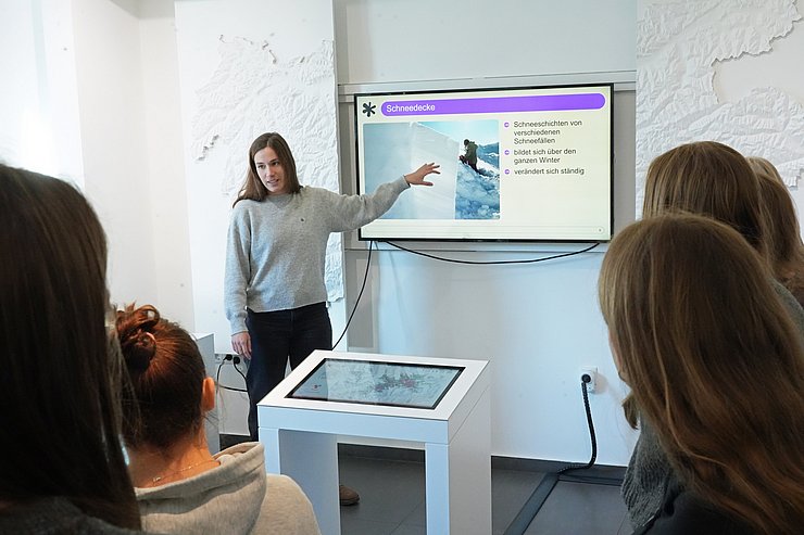 © Land Tirol/Pölzl Frau vor Fernseher redend und erklärend, SchülerInnen hören zu