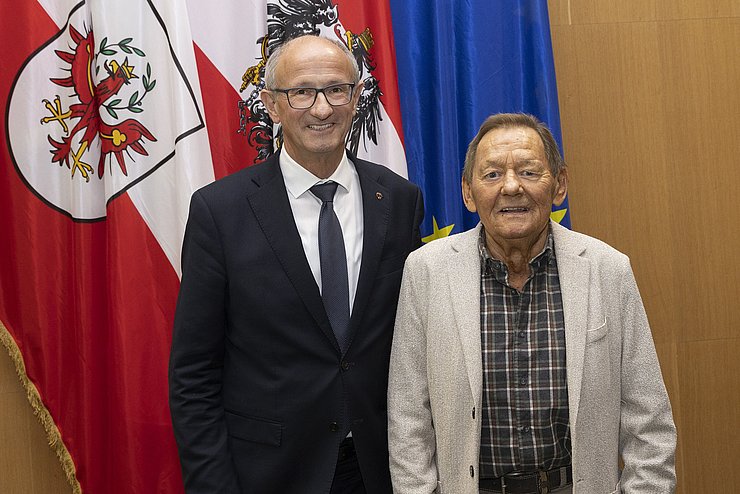 Anton Mattle steht mit Wolfgang Ambros vor der Tiroler Fahne.