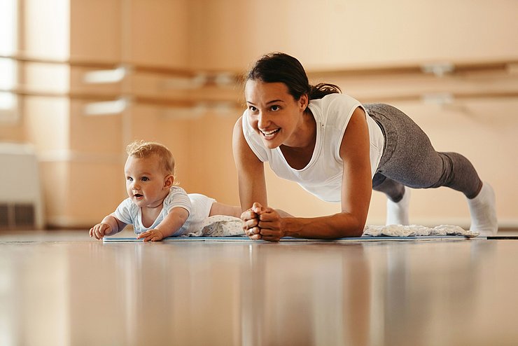 Junge Frau in Plank-Position, neben ihr ein Baby