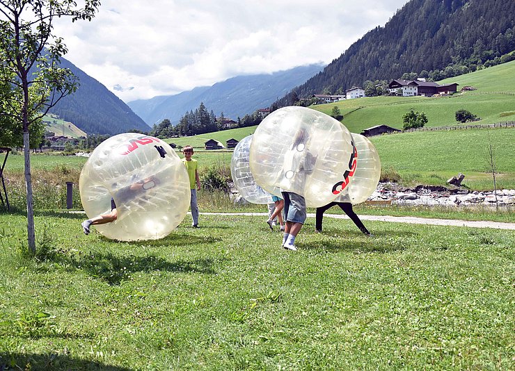 Vier Jugendliche, die auf einer Wiese in Gummibällen stecken und damit spielen.