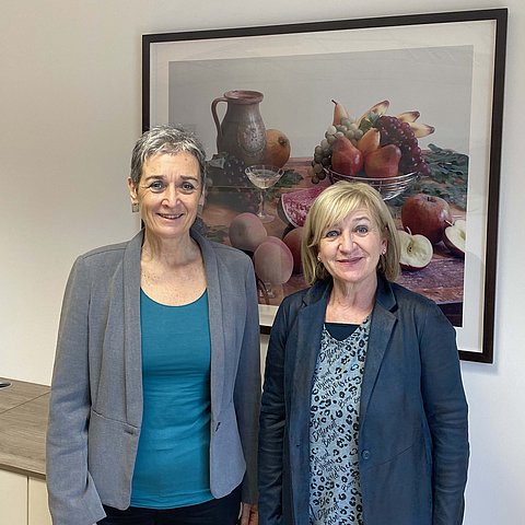 Kulturstaatssekretärin Ulrike Lunacek und Kulturlandesrätin Beate Palfrader stehen vor einem Gemälde im Staatssekretäriat. 