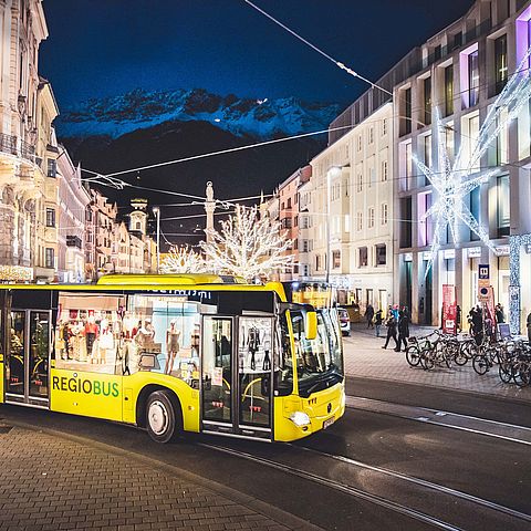 Fahrender Bus auf der Anichstraße vor dem Kaufhaus Tyrol bei Nacht
