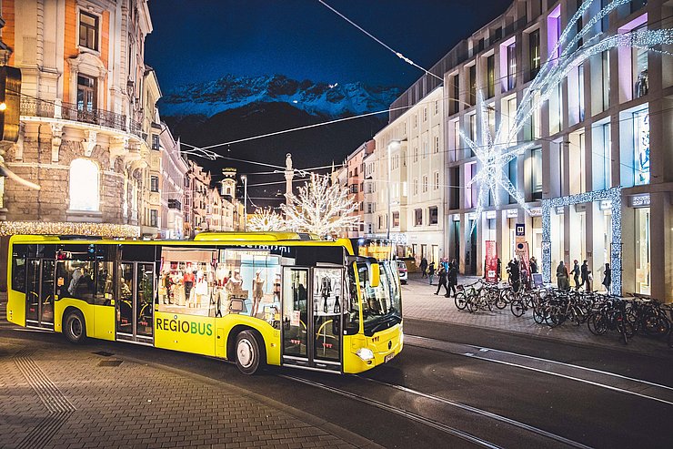 Fahrender Bus auf der Anichstraße vor dem Kaufhaus Tyrol bei Nacht