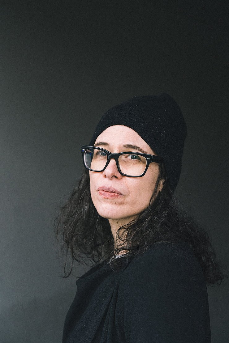 Eine Frau mit dunklen locken und schwarzer Brille.