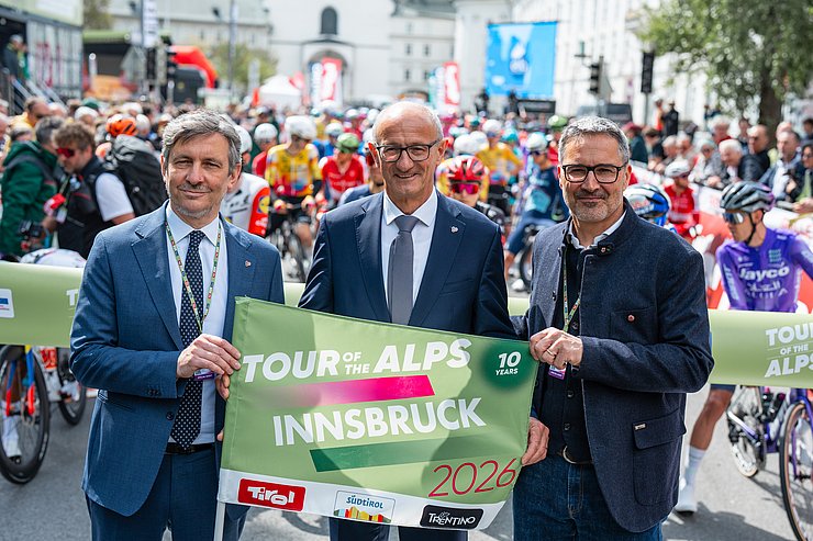 © Land Tirol/Fitsch Personen halten Plakat, dahinter RadsportlerInnen