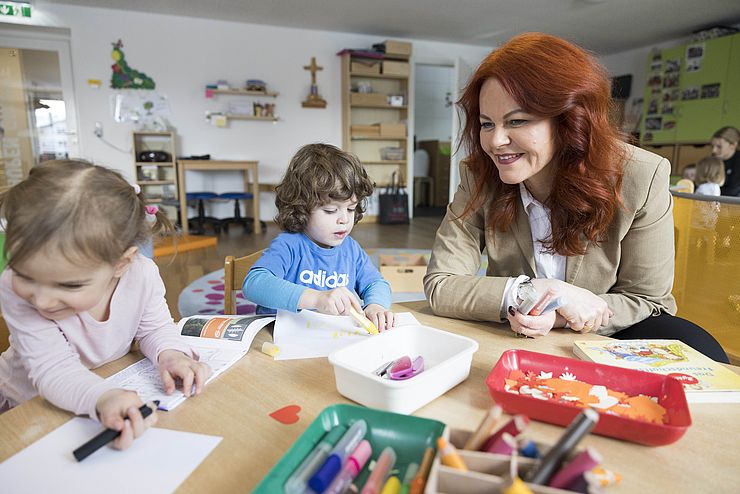 LRin Hagele sitzt mit zwei Kindern einer Kindergruppe an einem Tisch und malt Bilder