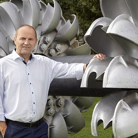 Landeshauptmann-Stellvertreter Geisler an einer Turbine angelehnt. Hinter ihm befindet sich eine weitere Turbine.