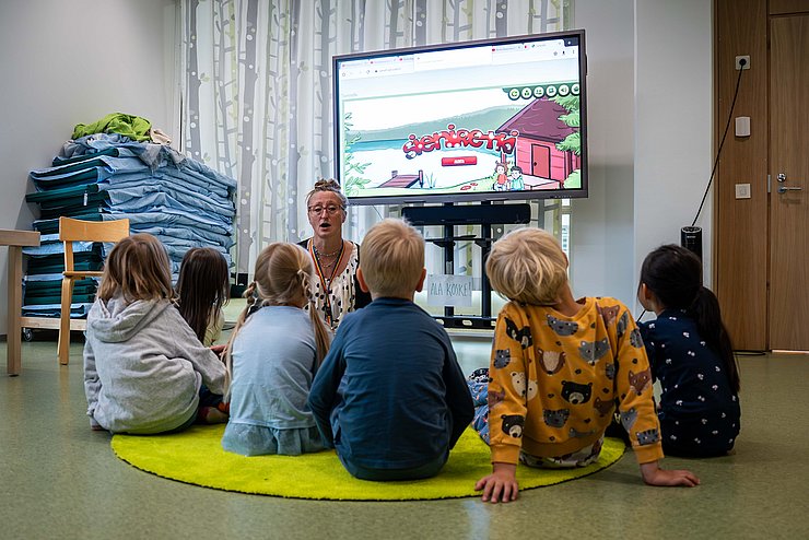 Betreuerin und Kinder auf Boden sitzend spielen