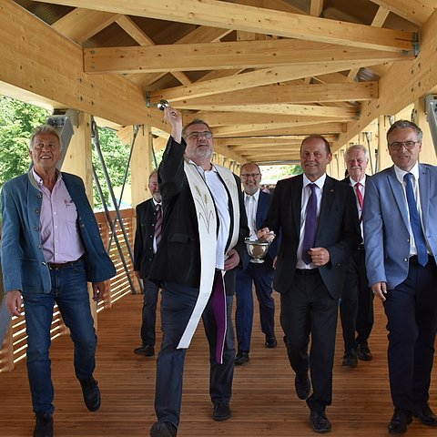 ein Foto von Bgm von Oberaudorf Alois Holzmaier, Pfarrer Thomas Schwarzenberger, LHstv. Josef Geisler und Bgm von Erl Georg Aicher-Hechenberger bei der Segnung des neuen Erler Innstegs wie sie über die Brücke gehen