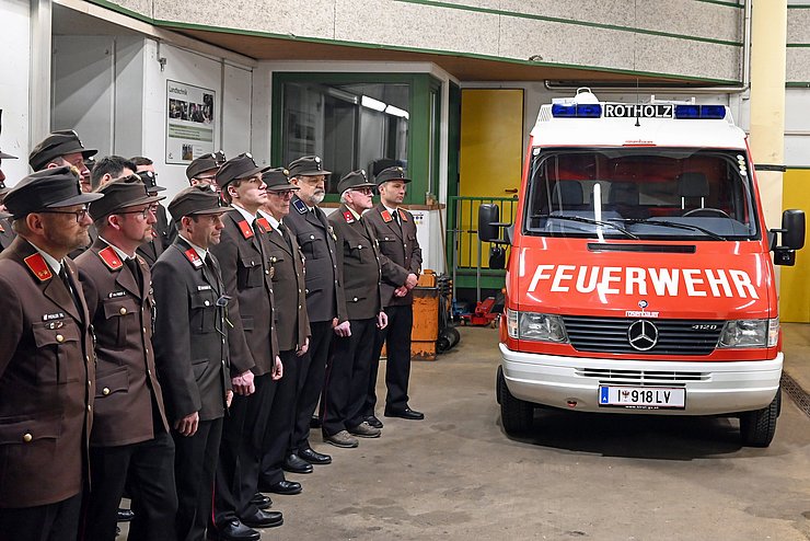 Gruppe Feuerwehrleute in Formation stehend; daneben Feuerwehrauto