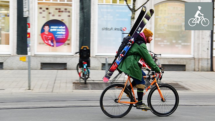 Ein Radfahrer fährt mit Rourenskiern am Rücken durch die Stadt.
