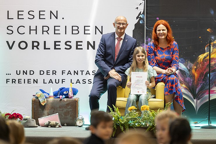 53 Volksschulen nehmen beim landesweiten Geschichtenwettbewerb zum Vorlesetag 2026 teil (im Bild: LH Anton Mattle und LRin Cornelia Hagele mit Vorjahressiegerin Theresa Haider).