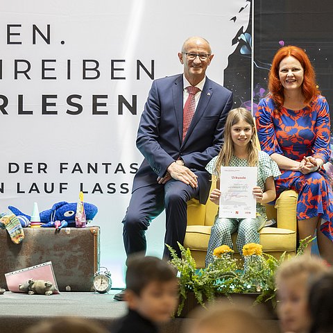 53 Volksschulen nehmen beim landesweiten Geschichtenwettbewerb zum Vorlesetag 2026 teil (im Bild: LH Anton Mattle und LRin Cornelia Hagele mit Vorjahressiegerin Theresa Haider).