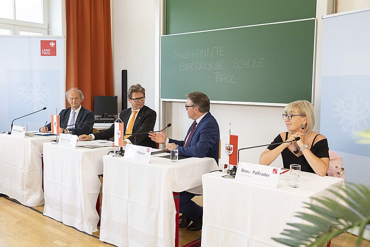 Vor der Tafel im Klassenzimmer jeweils an einer Schulbank sitzend