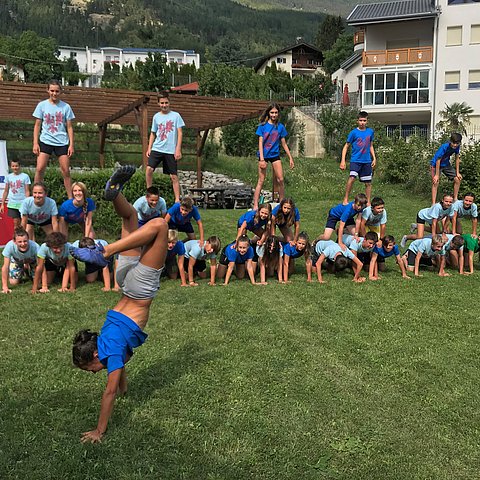 Kind vorne macht Handstand, hinten weitere Kinder aufgereiht in Sportkleidung