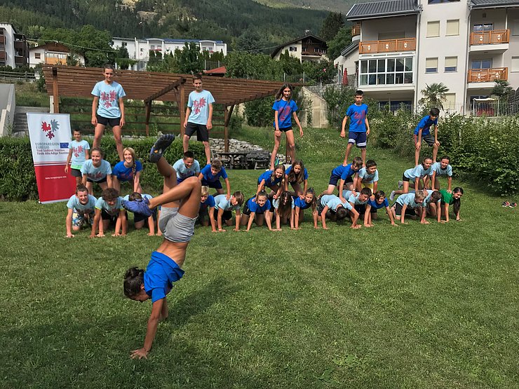 Kind vorne macht Handstand, hinten weitere Kinder aufgereiht in Sportkleidung