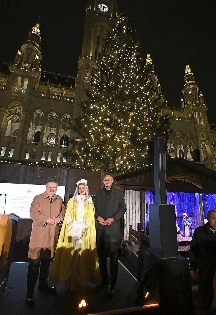 Personen stehen vor erleuchtetem Christbaum