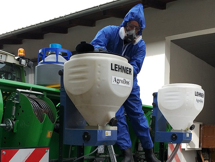 eine Person in Schutzkleidung befüllt einen Granulatstreuer, welcher an einem Traktor montiert ist