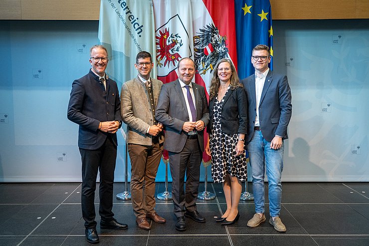 © Land Tirol/Neuner Fünf Personen stehen vor Fahnen.