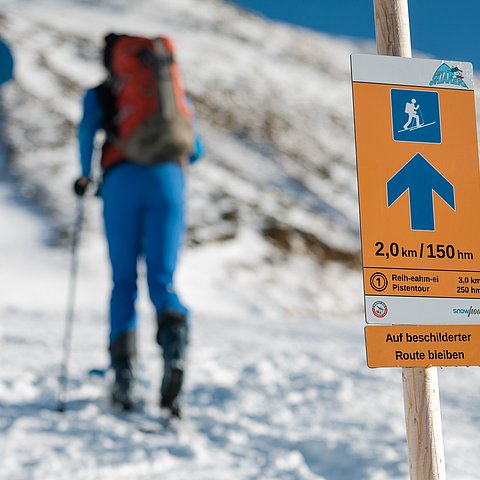 Beschilderung und im Hintergrund eine Frau in Pistenmontur 